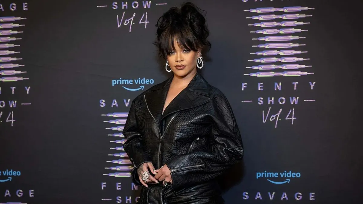 A female music artist rihanna height and fashion mogul with an elegant upswept hairstyle and bangs, wearing an oversized black crocodile-textured leather jacket and large diamond hoop earrings, posing confidently at the Savage X Fenty Show Vol. 4 event backdrop for Amazon Prime Video.