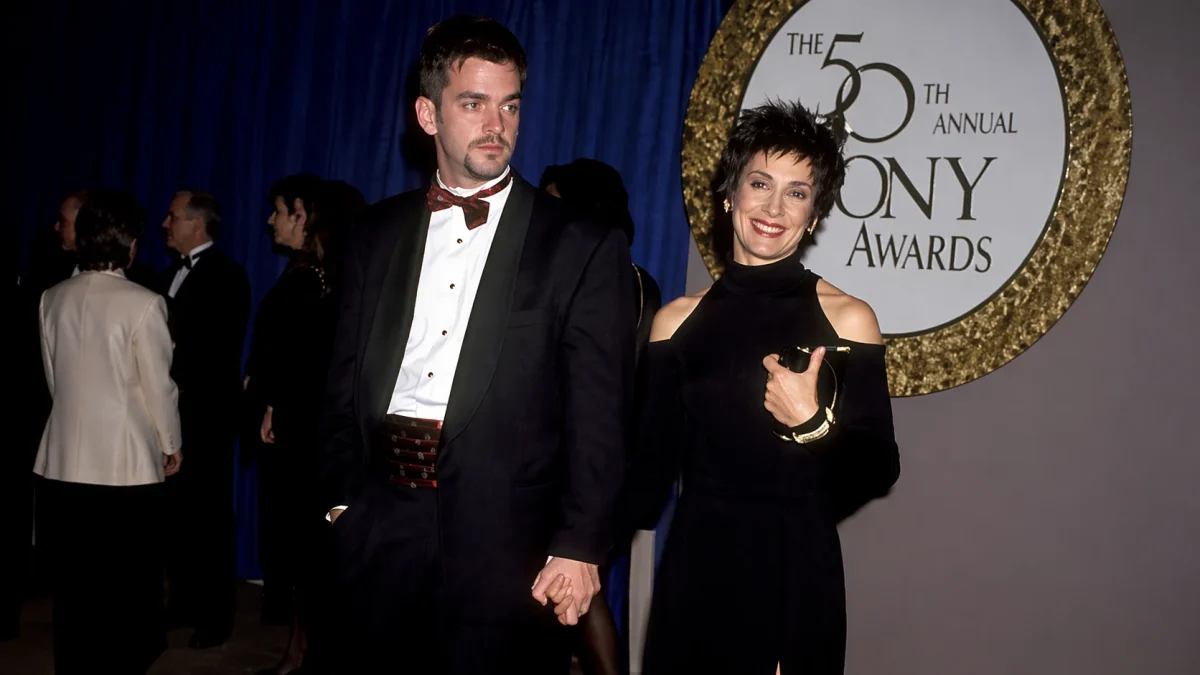 A young man in a black tuxedo with a burgundy bow tie and cummerbund holding hands with a smiling dark-haired woman in a black cold-shoulder dress at the 50th Annual Tony Awards of Will Theron Roth ceremony backdrop.