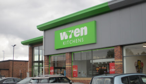 Wren Kitchens Chapter 7 showroom exterior with green signage, large windows, and parked cars outside on a cloudy day.
