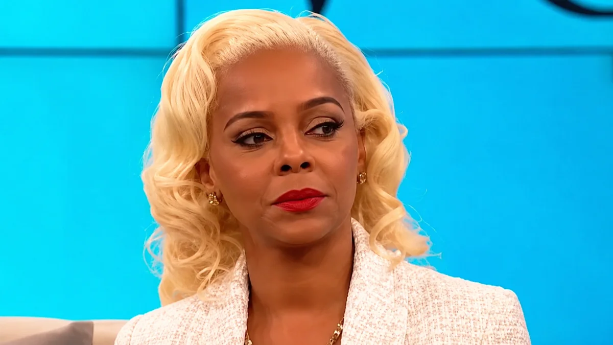 Close-up portrait of a blonde woman with styled hair, red lipstick, and elegant attire against a blue studio background, Lark Voorhies Net Worth related visual representation.