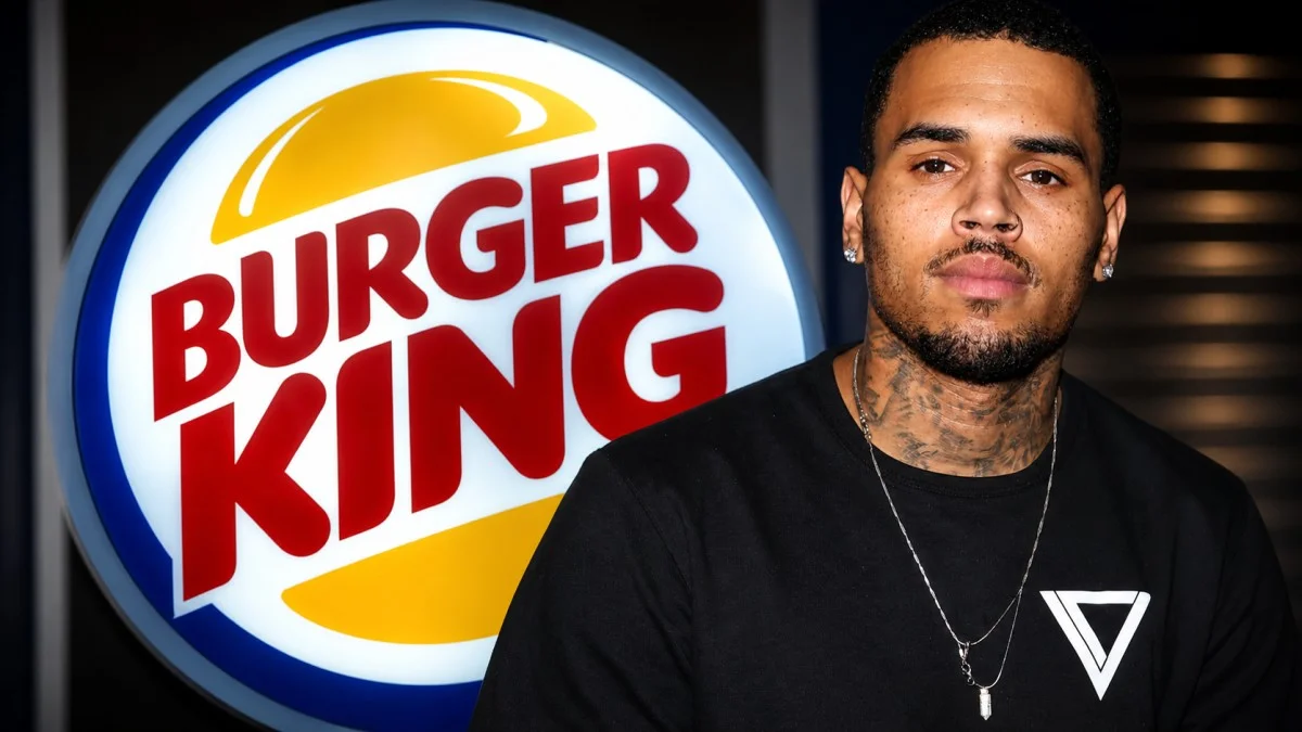 Chris Brown in a black t-shirt and silver chain necklace posed in front of an illuminated Burger King logo sign, representing the fast food franchise investment that diversifies Chris Brown net worth beyond his music and entertainment career earnings.