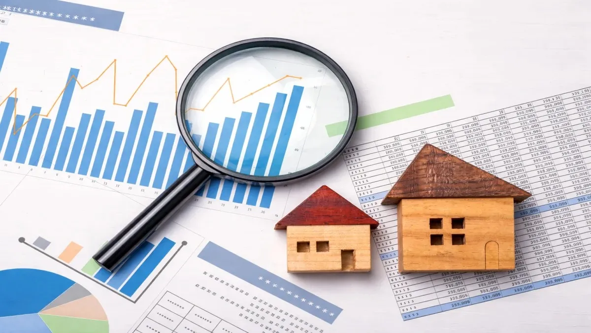 A magnifying glass over financial growth charts and small wooden houses, used as a conceptual visual for analyzing the Christopher Nolan net worth and his real estate investments.