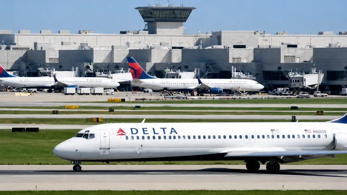 Delta flight airplane taxiing on runway with airport terminal and control tower in background