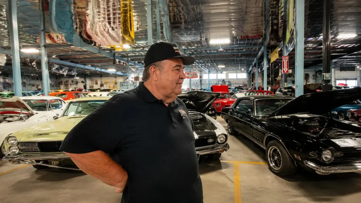 Don Baskin walking through a classic car museum filled with vintage vehicles – Don Baskin Net Worth