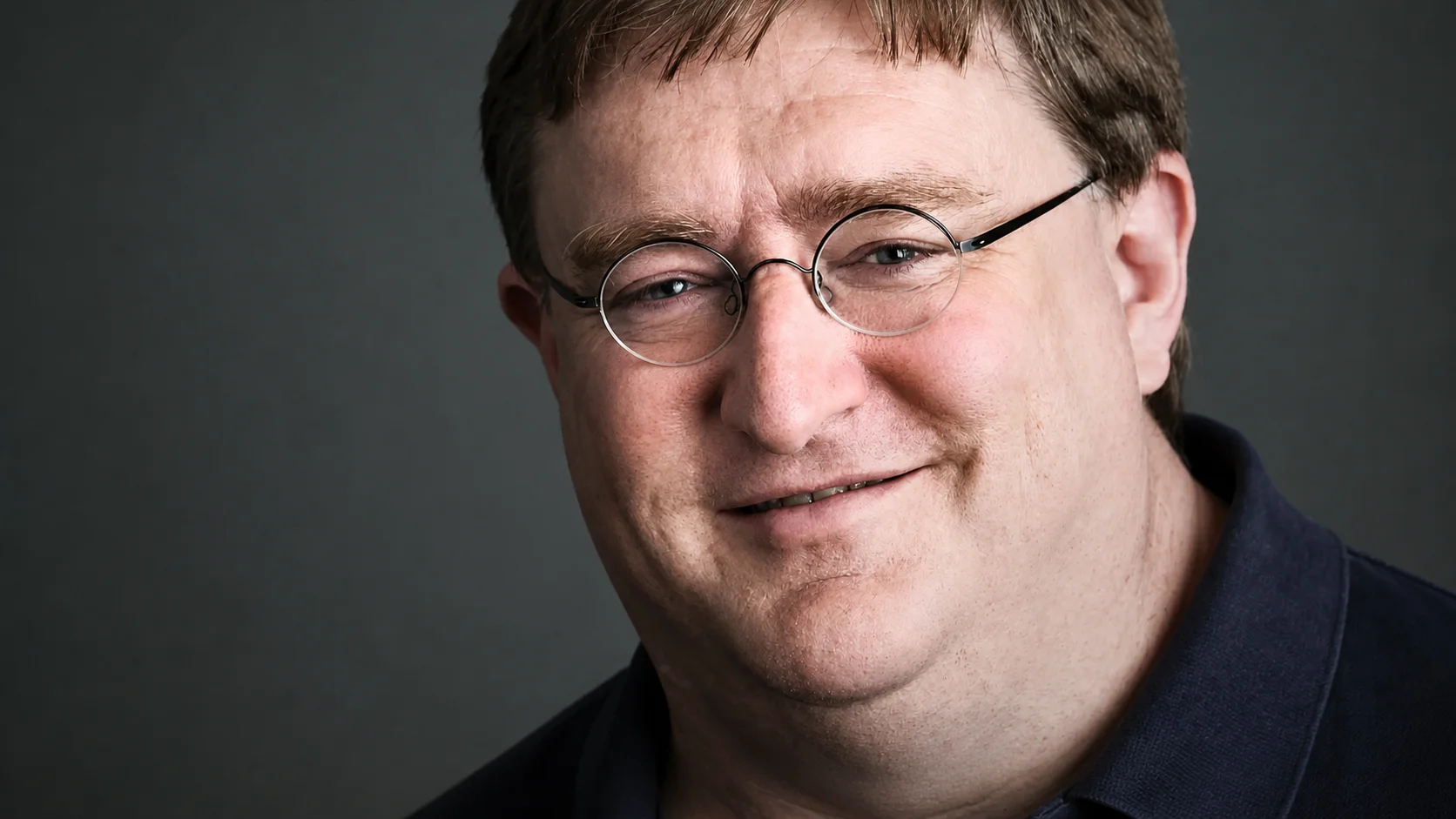 Portrait of Gabe Newell, founder of Steam, wearing glasses and smiling in a studio setting
