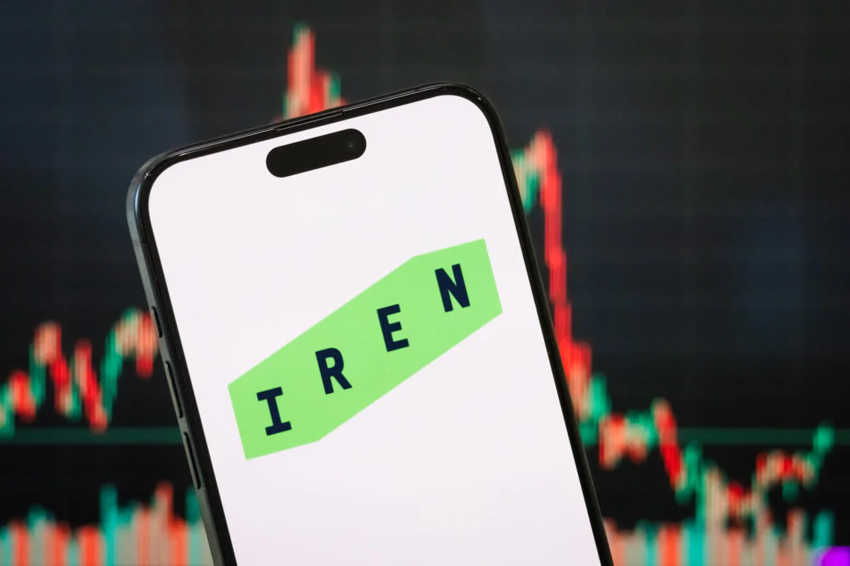 IREN stock logo shown on an iPhone screen with a red and green candlestick trading chart visible in the background