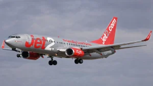 A Jet2 pilot landing a silver and red Boeing 737 aircraft with landing gear down on final approach against a cloudy sky