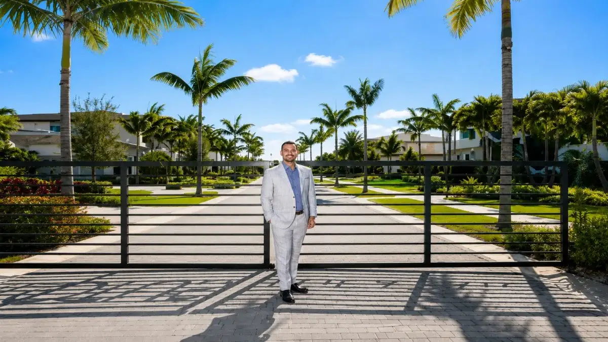 Misha Ezratti standing at a luxury gated estate entrance with palm trees – Misha Ezratti Net Worth