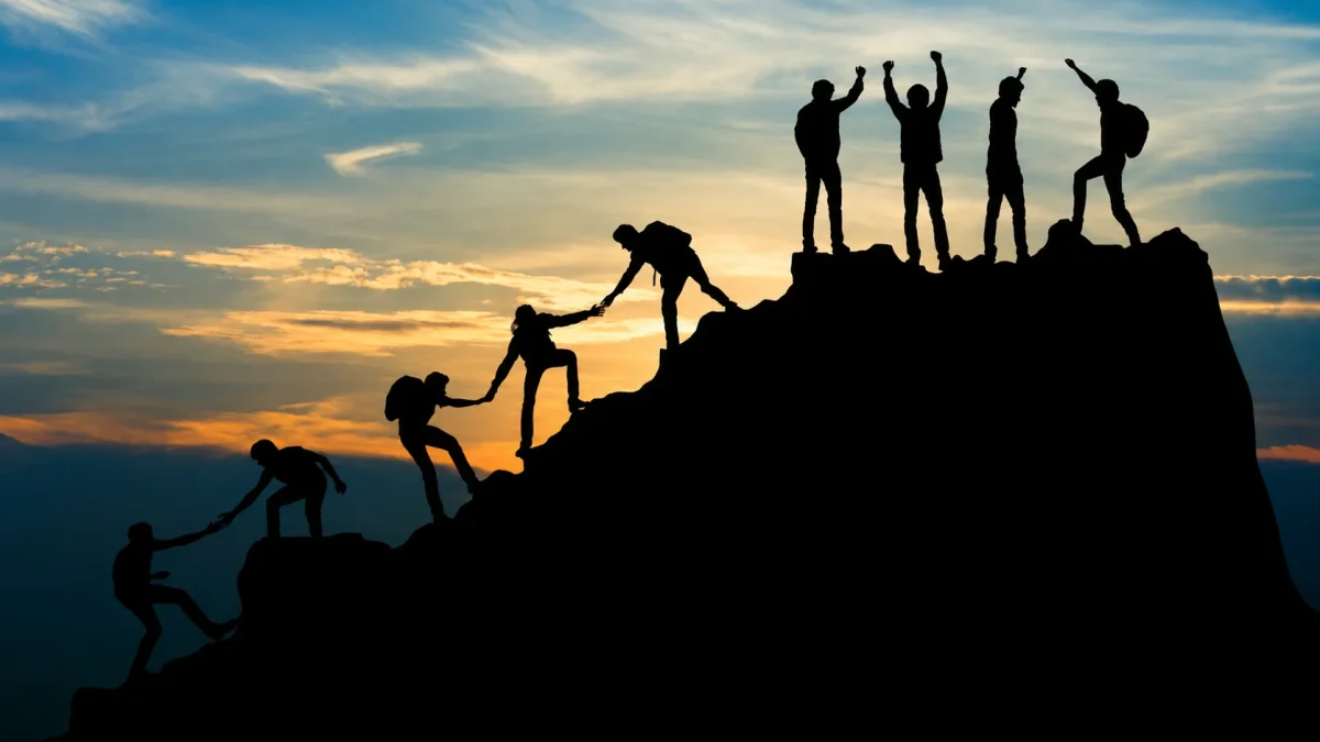 Gabe Newell inspired silhouette of people helping each other climb a mountain at sunset, symbolizing teamwork and leadership.
