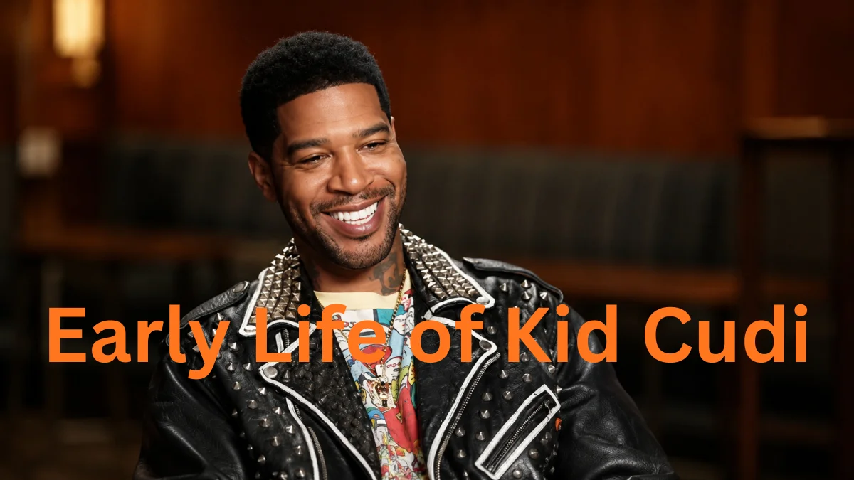 A smiling Kid Cudi wearing a studded black leather jacket over a graphic t-shirt during an interview, highlighting the humble beginnings of his early life that eventually built the substantial Kid Cudi Net Worth.